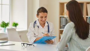 Mujer médica sonriente toma notas mientras conversa con una paciente en un consultorio iluminado