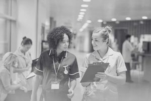 Enfermeras latinoamericana y europea conversando en un hospital mientras revisan documentación clínica.